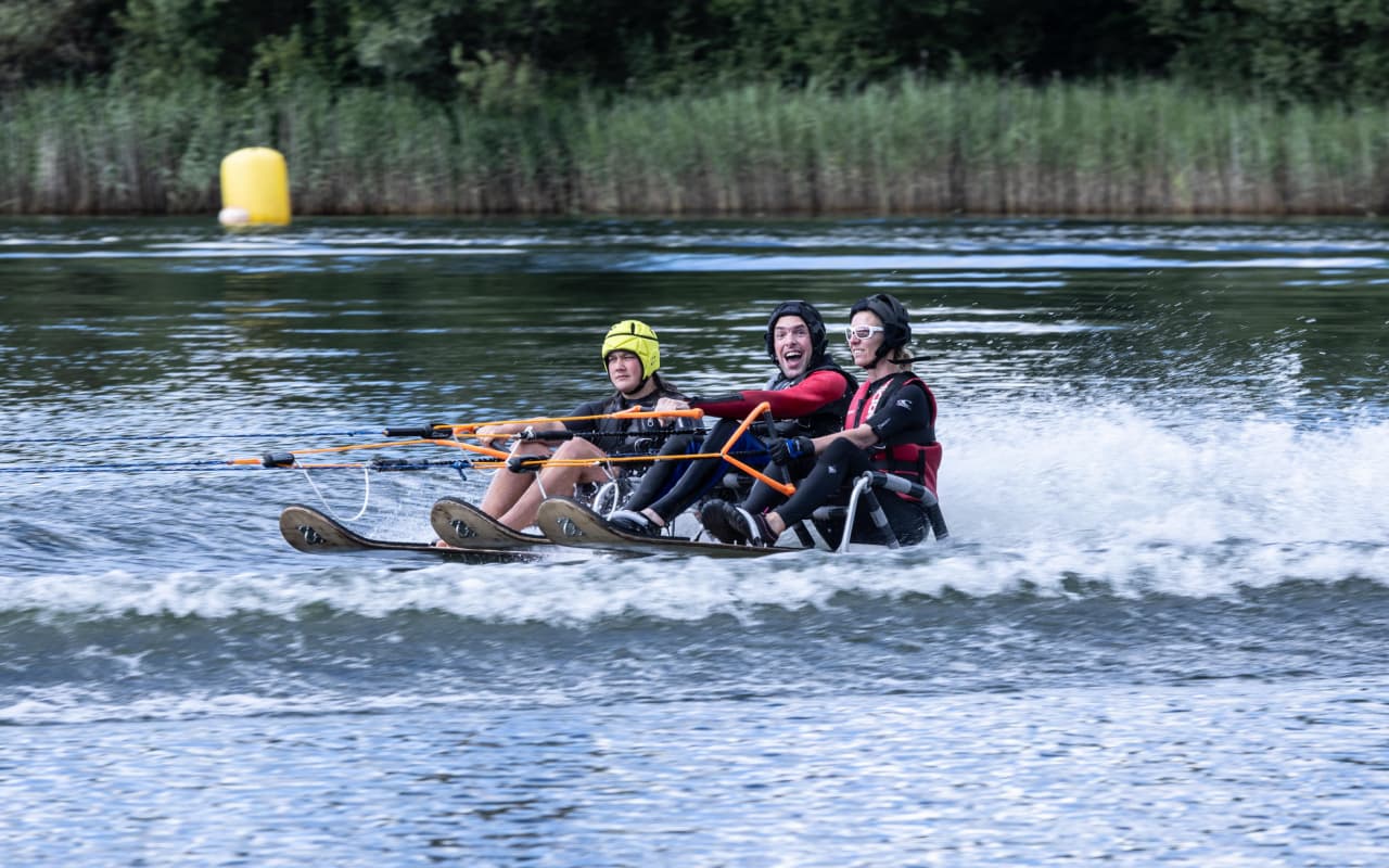 Three people having run while riding a board that is being pulled along by a boat